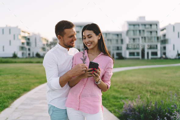 Boyfriend presenting flowers to girlfriend with smartphone