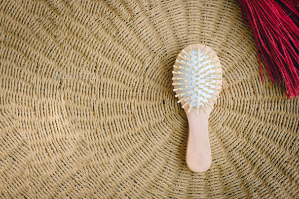 Small round wooden natural hair comb against the background of a wicker basket. Hair care.