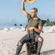Portrait of cheerful young man waving hello seated on his luggage in south beach - PhotoDune Item for Sale
