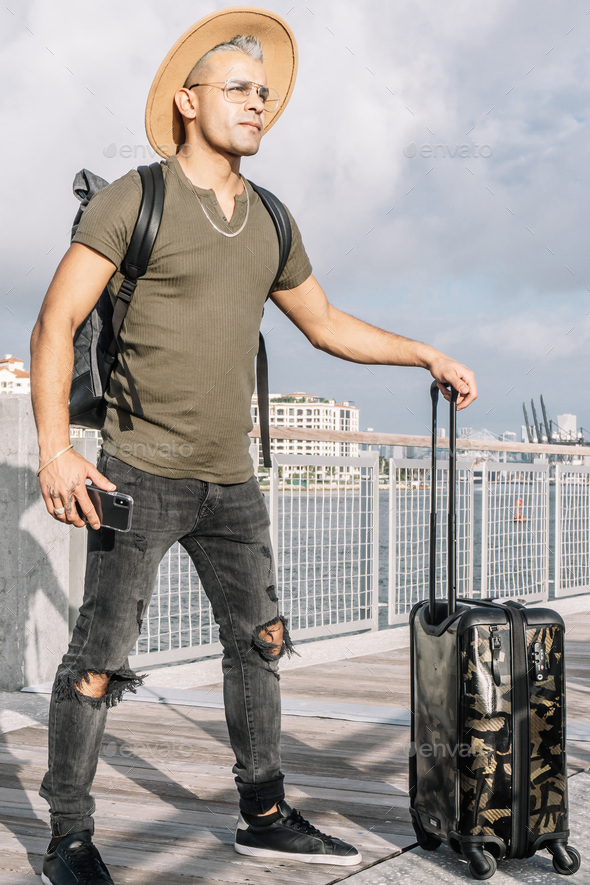 Portrait of a traveller man holding a smartphone and a carrying suitcase - Stock Photo - Images
