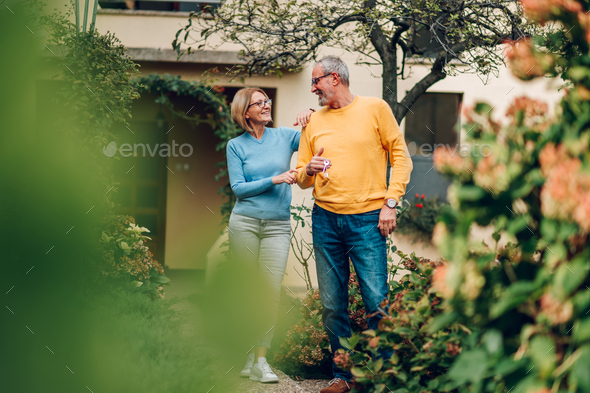 Senior couple holding keys and standing outside their new home - Stock Photo - Images