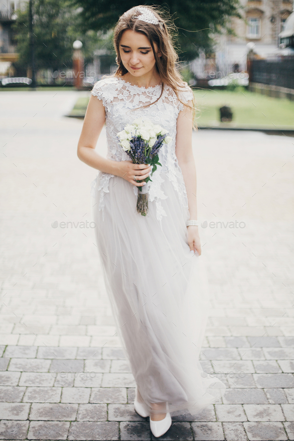 Sensual bride in stylish gown walking with wedding bouquet of roses and lavender. Provence wedding