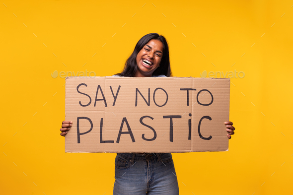 Say no to plastic. Happy Indian woman holding cardboard poster looking at camera. yellow background.