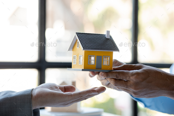 A housing salesman holds a model of a house and sends it to customers as an example.