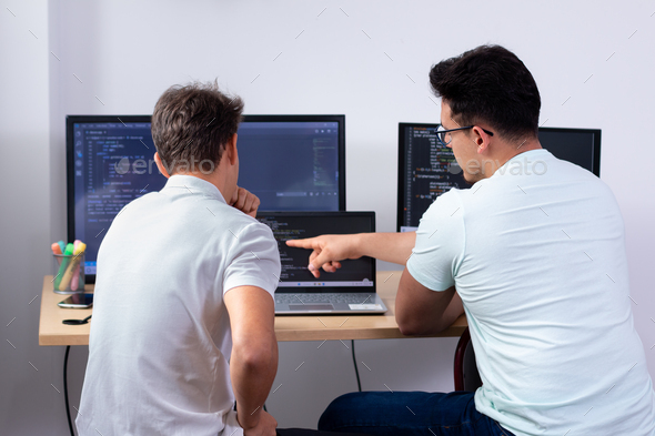 Programmers looking for bugs in the code together on a computer with three monitors.