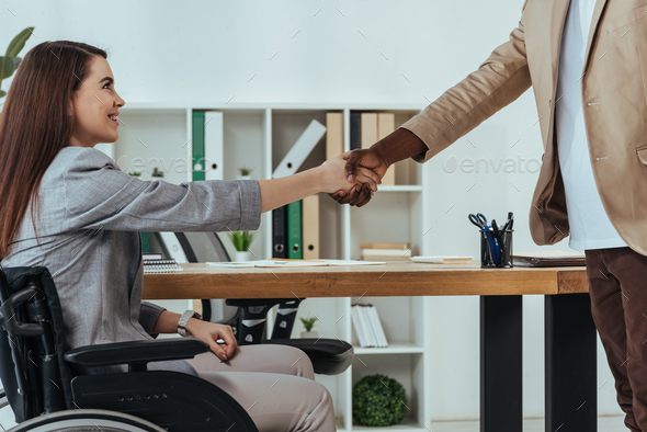 Disabled employee and african american recruiter shaking hands at job interview in office