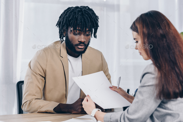 Selective focus of recruiter looking at paper near worried african american employee at job