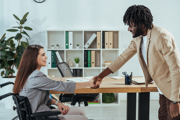 Disabled employee and african american recruiter shaking hands at job interview in office