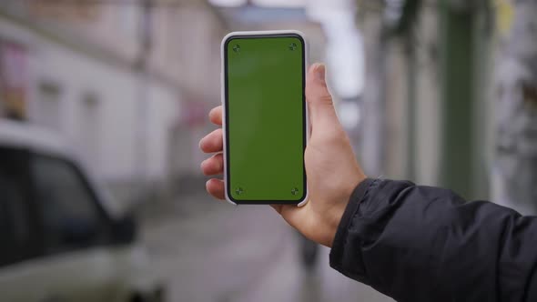 Hand Man Uses Holding a Mobile Telephone with a Vertical Green Screen Background on of Street Houses