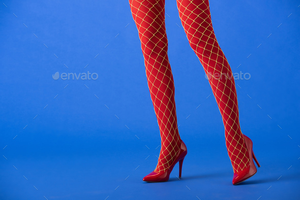 cropped view of woman in fishnet tights and red heels posing on