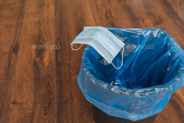 blue medical mask in trash can with garbage bag, end of quarantine concept