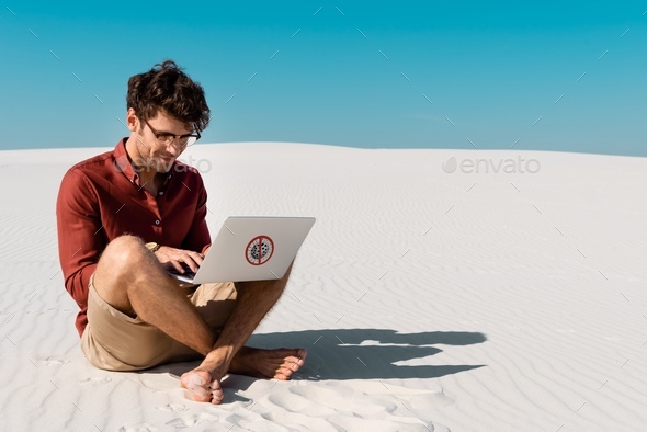 young freelancer on sandy beach using laptop with stop virus sign against clear blue sky