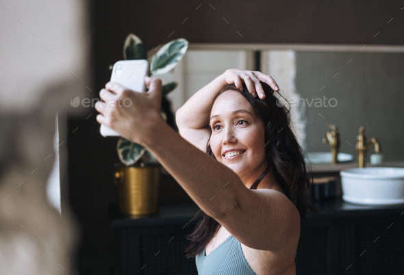 Self loving middle aged woman in underwear taking selfie with mobile phone in bathroom at home - Stock Photo - Images