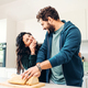 A young caucasian couple in their 30s shares a laugh while they eat bread in a modern, bright kitche - PhotoDune Item for Sale