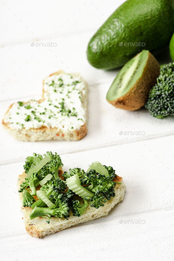 selective focus of heart shaped canape with creamy cheese, broccoli, microgreen near green fruits - Stock Photo - Images