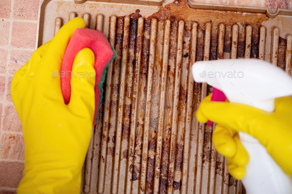 Man cleaning grilled pan or electric grill with detergent agent. Hands in yellow gloves