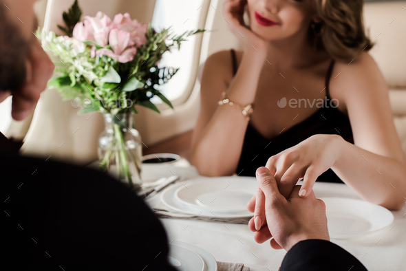 selective focus of man and woman holding hands while sitting at served table in plane - Stock Photo - Images