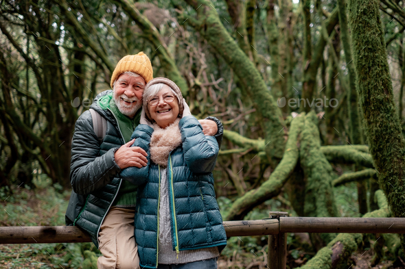 Cheerful senior couple enjoying nature outdoors in a mountain forest with moss covered trunks