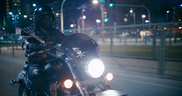 Motorcyclist All in Black Rides Motorbike on City Roads at Night with Lights
