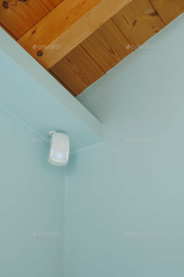 Motion sensor or detector for security system mounted on blue wall in mansard with wooden ceiling