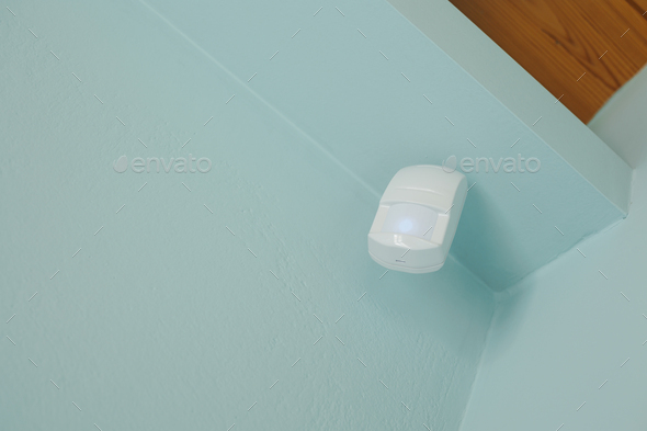 Motion sensor or detector for security system mounted on blue wall in mansard with wooden ceiling