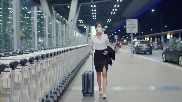 Asian business girl arrive destination wear face mask with drag luggage walk outside wait car.