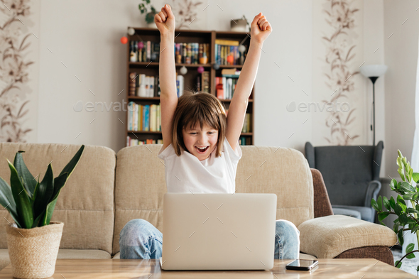 Online distance learning for children at home. The girl sits on the couch in front of a laptop  - Stock Photo - Images