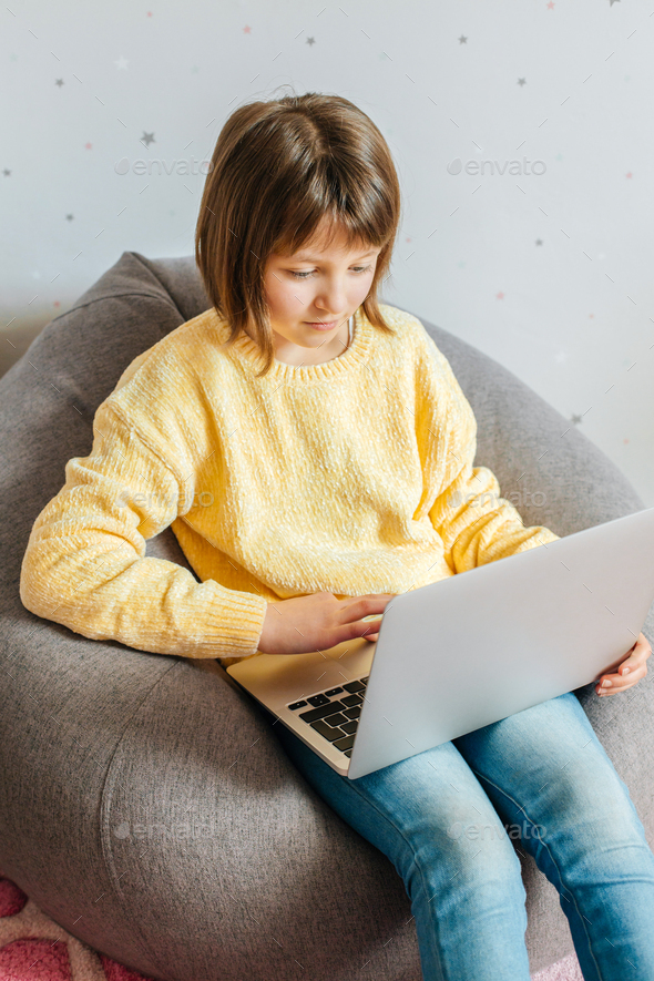 A girl sits in her room with a laptop on her lap and watches lessons or training courses. Children u - Stock Photo - Images
