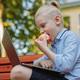 cute caucasian boy sitting on bench in park with laptop computer eating an apple - PhotoDune Item for Sale