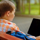 cute caucasian boy sitting on bench in park with laptop computer. Black screen - PhotoDune Item for Sale