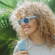 Portrait of young adult cheerful woman with a smile wearing blue sunglasses against a leaves - PhotoDune Item for Sale
