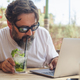 One young mature man with beard working on laptop while drinking mohito cocktail at the summer care - PhotoDune Item for Sale
