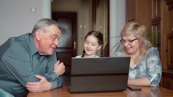 Young little school age girl teaching grandparents using laptop notebook tech at home