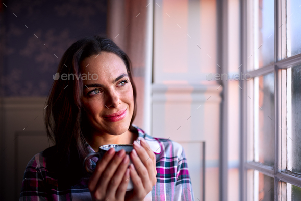 Woman At Home With Hot Drink Standing Looking Out Of Window With Evening Light - Stock Photo - Images