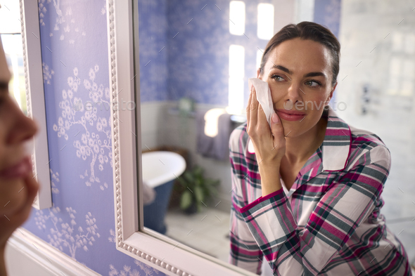 Woman At Home Wearing Pyjamas Looking In Bathroom Mirror Taking Off Make Up With Wipe - Stock Photo - Images