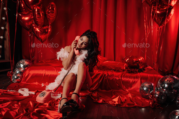 Portrait of smile sexy asian girl glam makeup in red lingerie sits near bed talking by retro phone - Stock Photo - Images