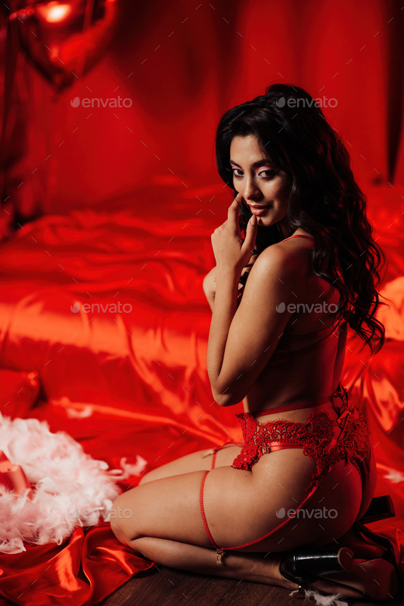 Portrait of smile sexy asian girl glam makeup in red lingerie sits near bed at valentines day decor - Stock Photo - Images