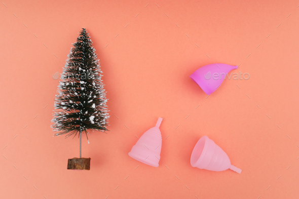 Pink menstrual cups and christmas tree on color background, female intimate hygiene period products