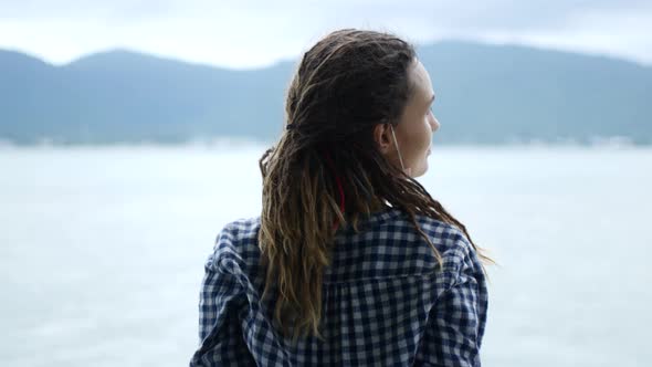 A Woman in Dreadlocks and a Mask Looks at the Sea a Rainy Day