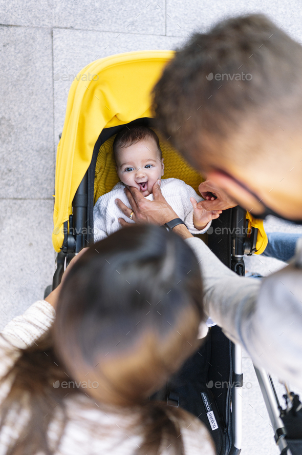 Caucasian couple looking and pinching the cheeks of their baby while he is in a baby stroller