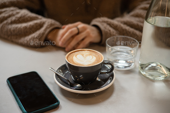Girl in cafe waits for call from loved one over cup of coffee with heart shaped latte art foam