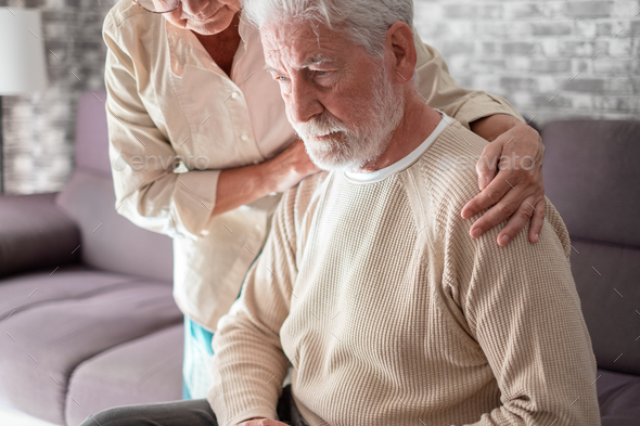 Senior woman comforting her depressed, mental ill husband, unhappy elderly man at home