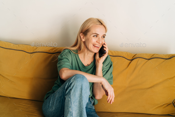 Attractive middle aged woman chatting cheerfully on the phone while sitting on the couch. - Stock Photo - Images