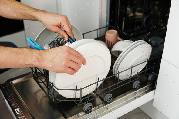 Washing dishes in the dishwasher. The man takes clean dishes from ...