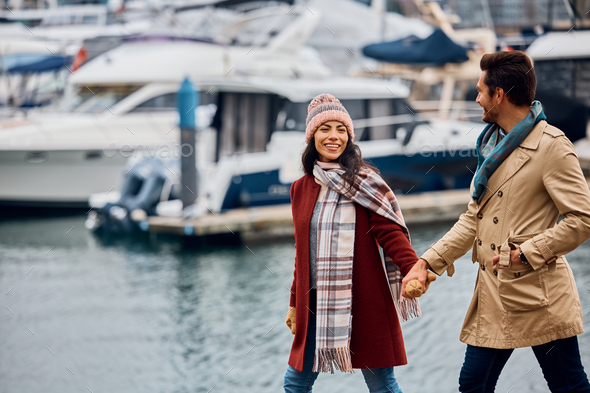Happy woman holding hands with her boyfriend while walking along a quay, - Stock Photo - Images