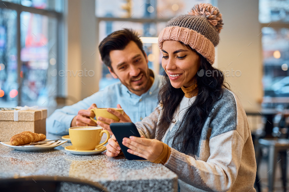 Happy woman using cell phone while drinking coffee with her boyfriend in a cafe. - Stock Photo - Images