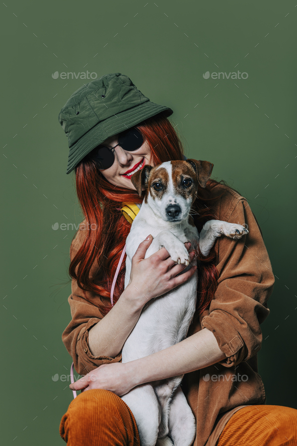 Stylish redhead woman with headphones and dog on green background - Stock Photo - Images