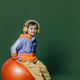 Stylish little boy in headphones sits on orange swiss ball on green background - PhotoDune Item for Sale