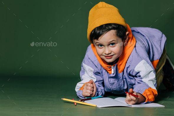 little boy lies on the floor and draws with pencils on green background - Stock Photo - Images