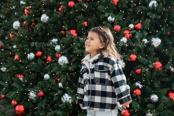 Lifestyle portrait of toddler girl smiling near Christmas tree  - Stock Photo - Images